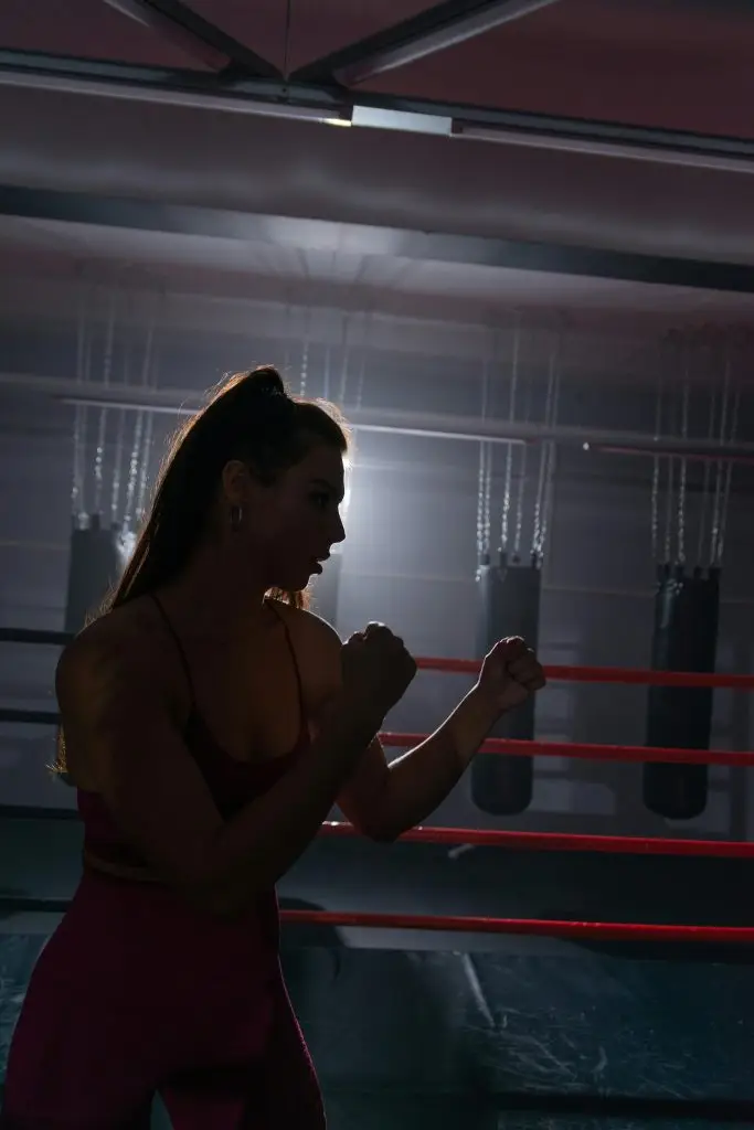 Silhouette of a female boxer practicing inside a dimly lit gym, showcasing strength and determination.